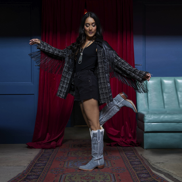 A woman wearing Justin Western boots while posing in front of a curtain.